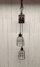 Load image into Gallery viewer, Two offset 5 1/2-inch diameter cage lamp shades housing Edison bulbs, suspended from a double wheel barn pulley, this pendant light hangs 36 inches, and has a 24-inch hanging chain.  Lights are not illuminated.
