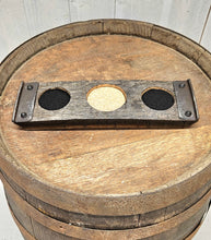 Load image into Gallery viewer, A whiskey barrel stave coaster sporting 3 indents.  The two at each end are covered in felt, and the middle one in cork.  There is a barrel ring fastened at each end of the coaster. The coaster sits on a barrel top. 
