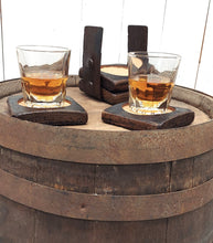 Load image into Gallery viewer, Front view of four coasters fashioned from whiskey barrel staves displaying two whiskey filled glasses on top of a rustic whiskey barrel.
